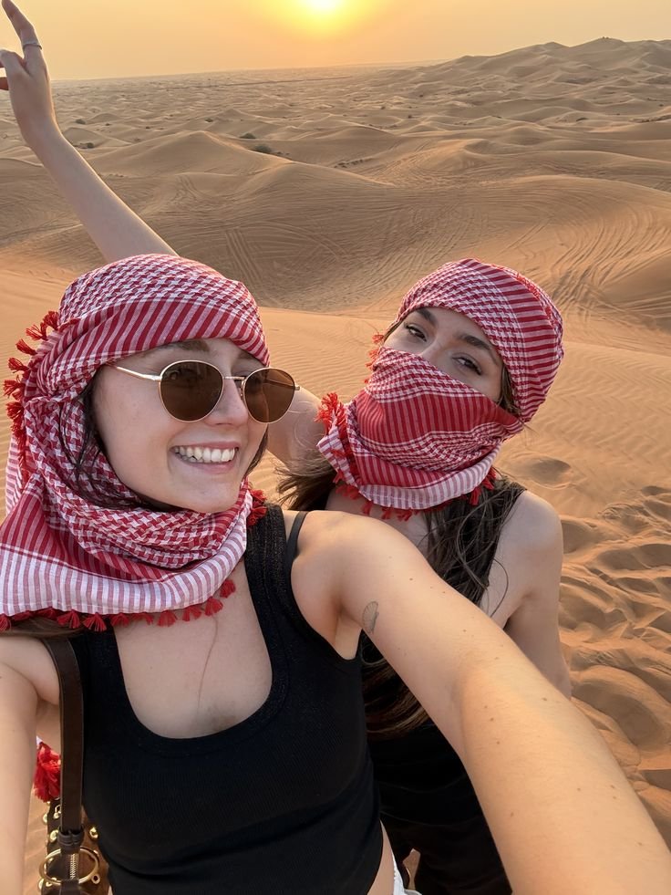 Two guests in keffiyeh taking a selfie on the dunes at sunset