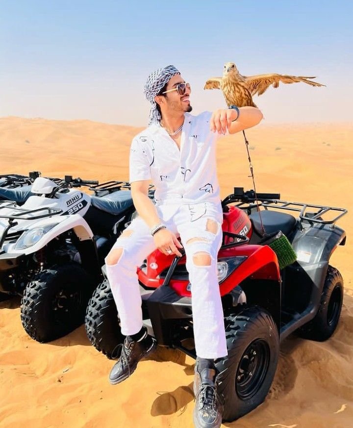 Guest holding a falcon while seated on a quad bike in the desert