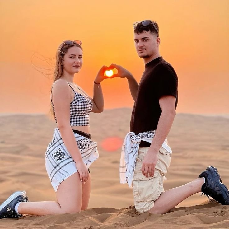 Couple framing the setting sun with their hands on the Al Khatim dunes