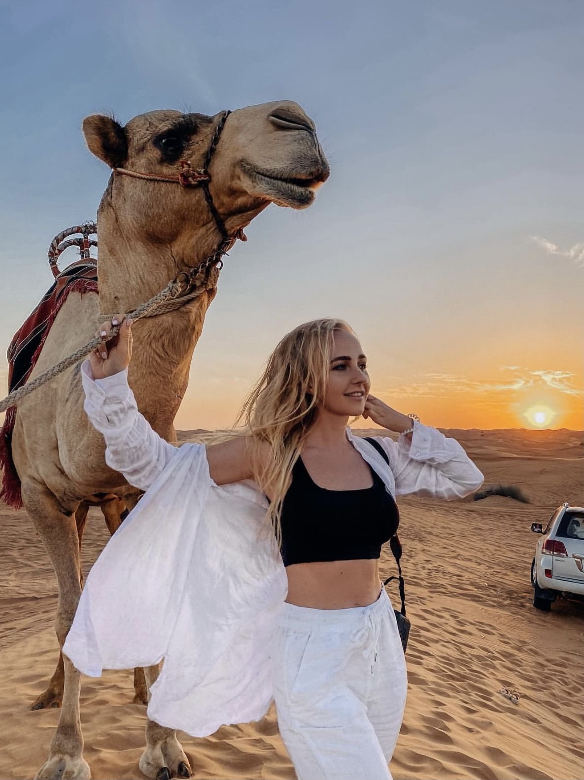 Guest leading a camel at sunset with the safari 4x4 behind – VIP desert safari Abu Dhabi