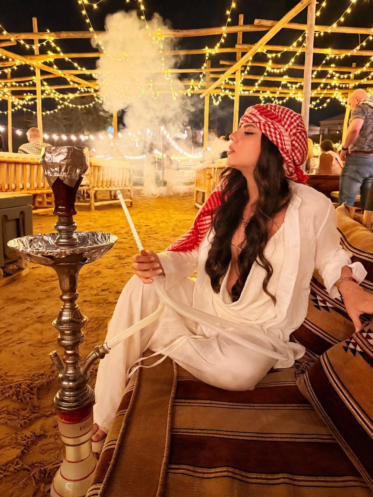Guest enjoying shisha under the festoon lights at the VIP desert camp